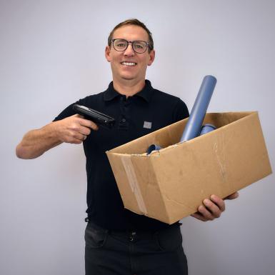 Porträt von Lagerleiter Roman Kössler mit Scanner und Materialschachtel