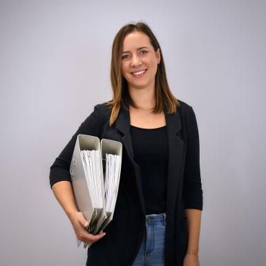 Porträt von  Büroassistentin Sarah Deuretzbacher mit Ordner unter dem Arm