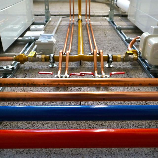 Ein Ensemble von Rohren unterschiedlicher Materialien und ein komplexes Kupferrohrverteilungssystem in einer technischen Umgebung.