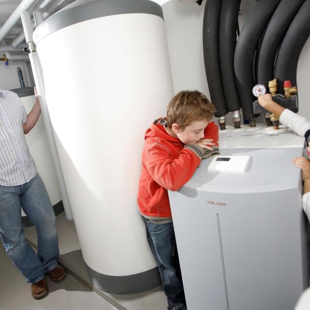 Ein Mann und zwei Jungen betrachten ein großes technisches Gerät mit vielen Rohren in einem gut beleuchteten Innenraum.